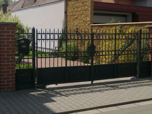Dvoukřídlá kovaná brána v černé barvě s plnou spodní výplní a lucernami na sloupcích