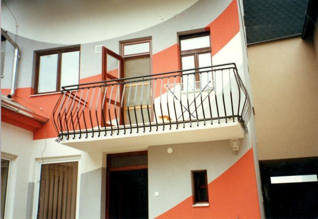 Černé kované balkónové zábradlí s obloukovými prvky na fasádě rodinného domu