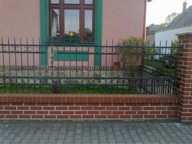 Pole kovaného plotu s kroužky a ornamenty na cihlové podezdívce