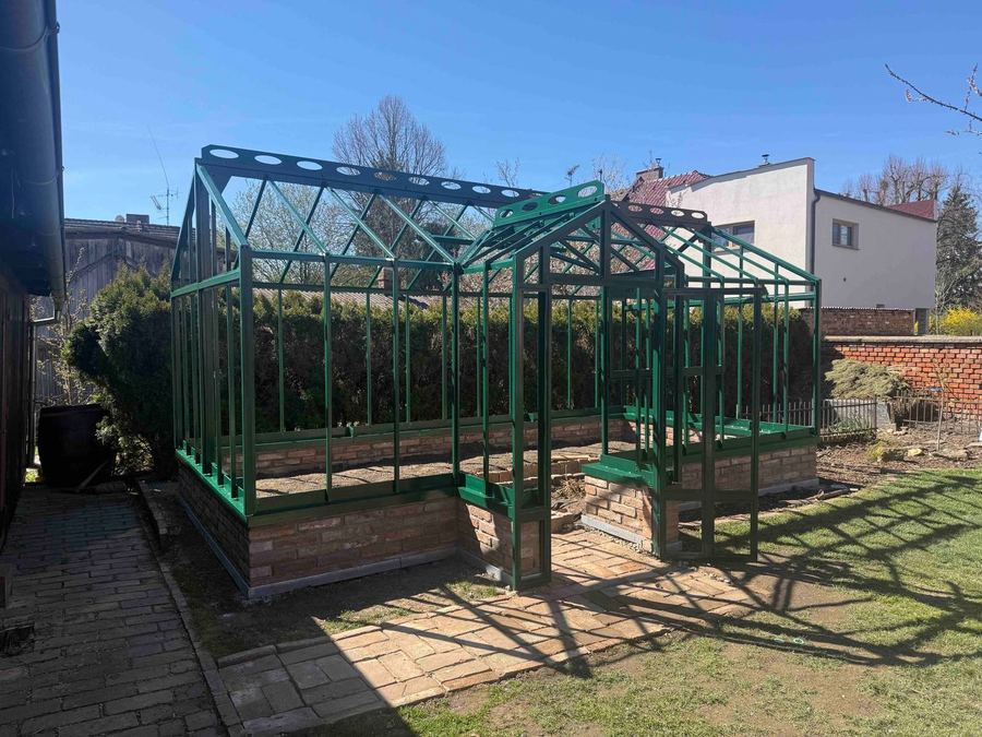 Ocelová konstrukce skleníku v zelené barvě na cihlové podezdívce před zasklením