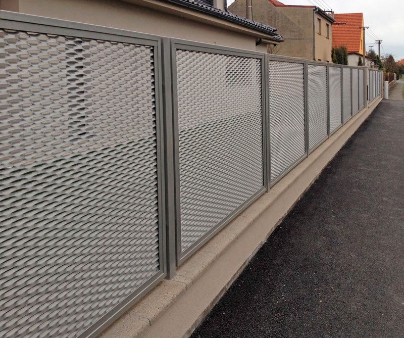 Plotová pole z tahokovu v šedé barvě na betonové podezdívce podél ulice