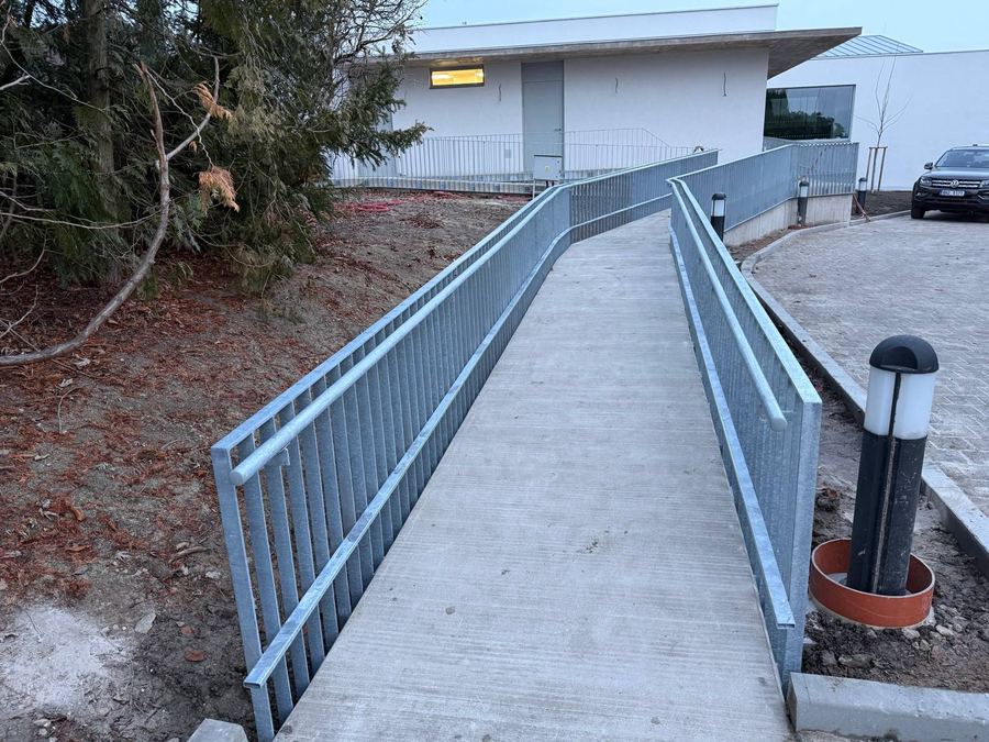 Zinkované ocelové zábradlí podél bezbariérové betonové rampy u nové budovy